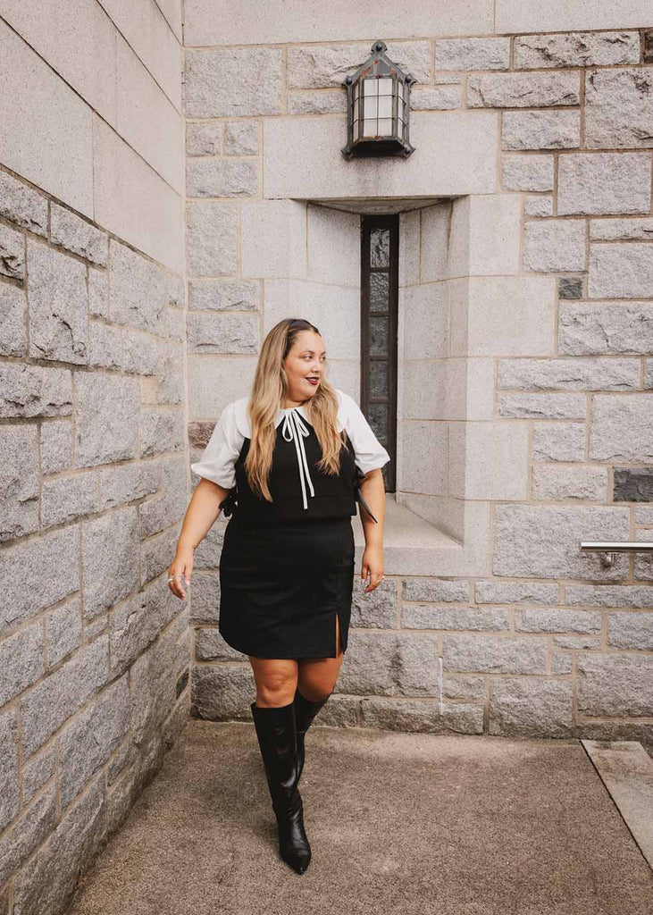 a plus size woman in a white blouse with an exaggerated collar layered with a black vest