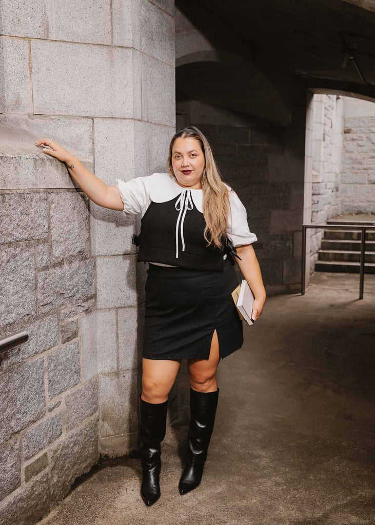 a plus size woman in a white blouse with an exaggerated collar layered with a black vest