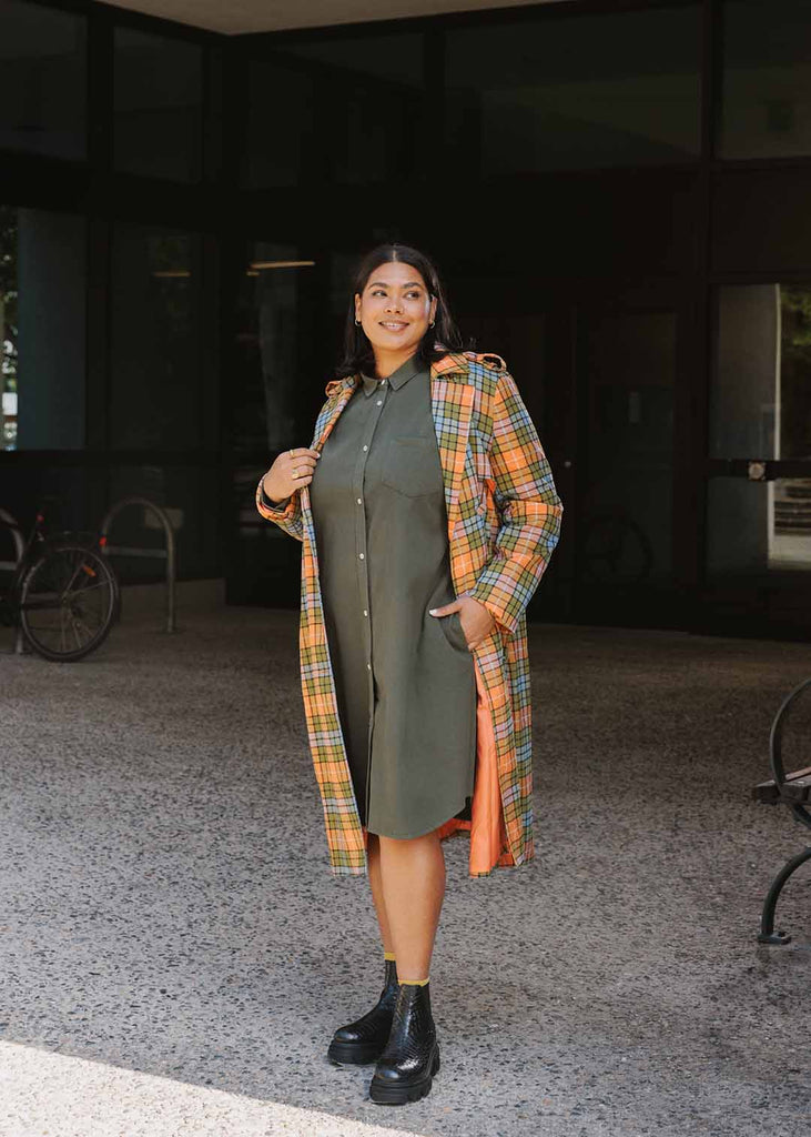 plus size person in an olive green shirt dress under an orange plaid trench coat