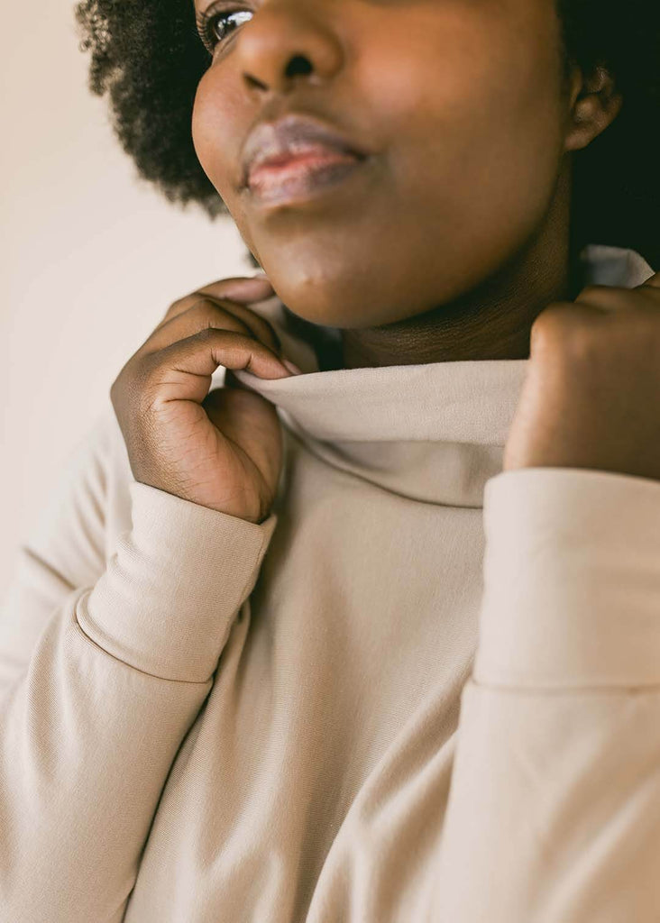 a close up of a woman wearing a cream rollneck sweatshirt