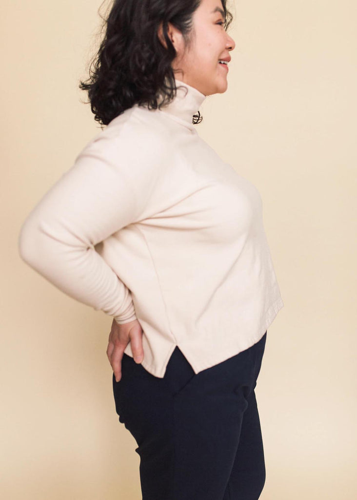 a mid size woman wearing a cream roll neck sweatshirt