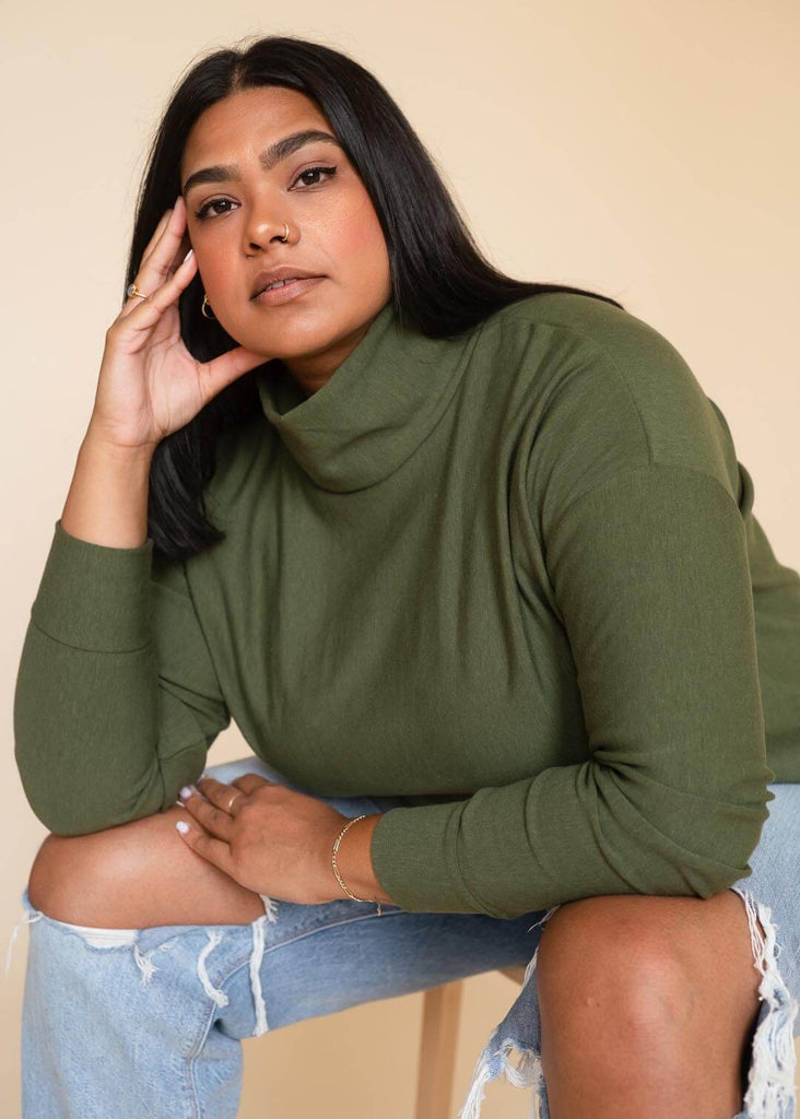 a plus size woman wearing a green roll neck sweatshirt